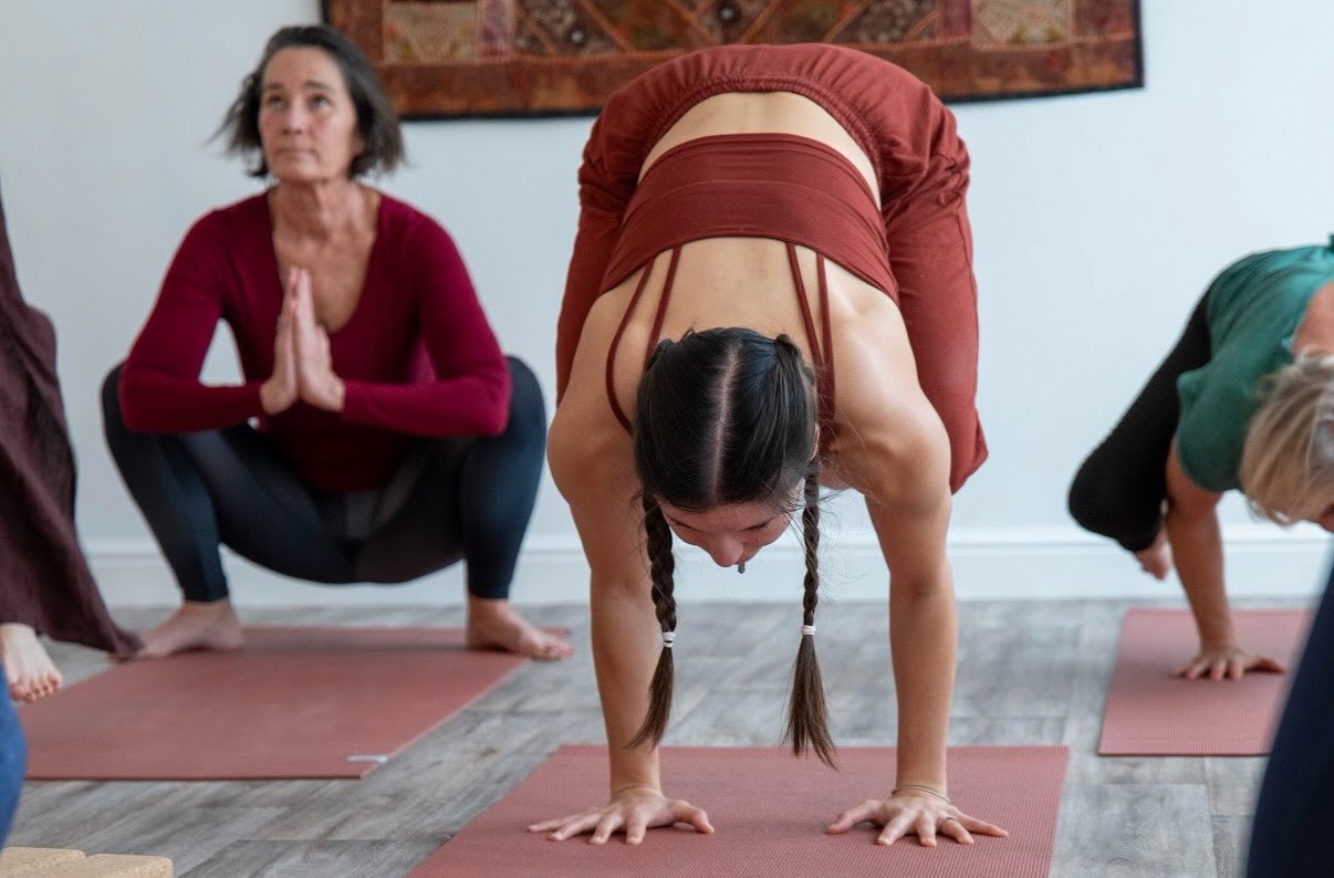 Students in a squat with hands at heart centre, and a forward fold